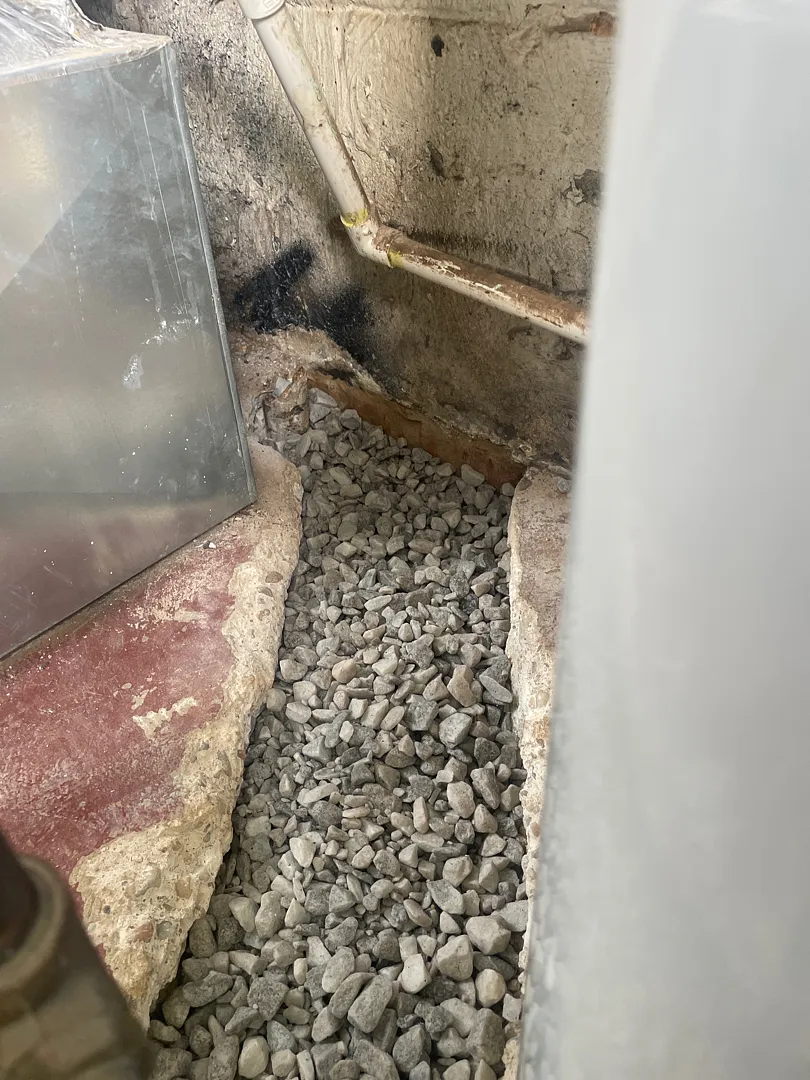 Drainage stone in a narrow interior foundation trench before concrete restoration
