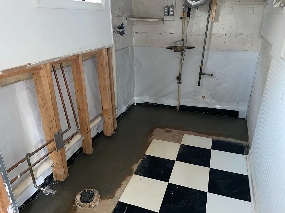 Fresh concrete restores the interior French drain trench while lower wall framing remains exposed