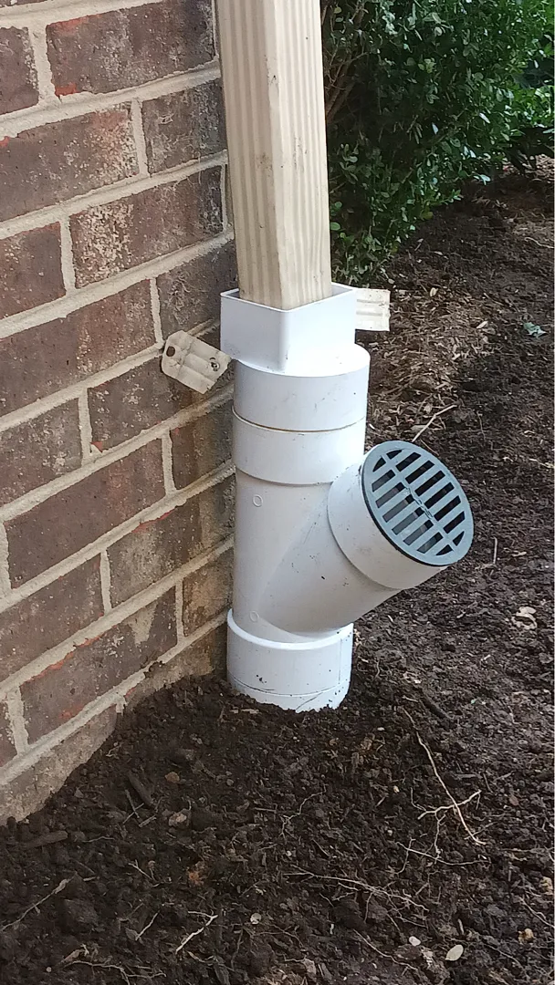 Downspout connection with grated branch beside a brick wall in Rockville, Maryland