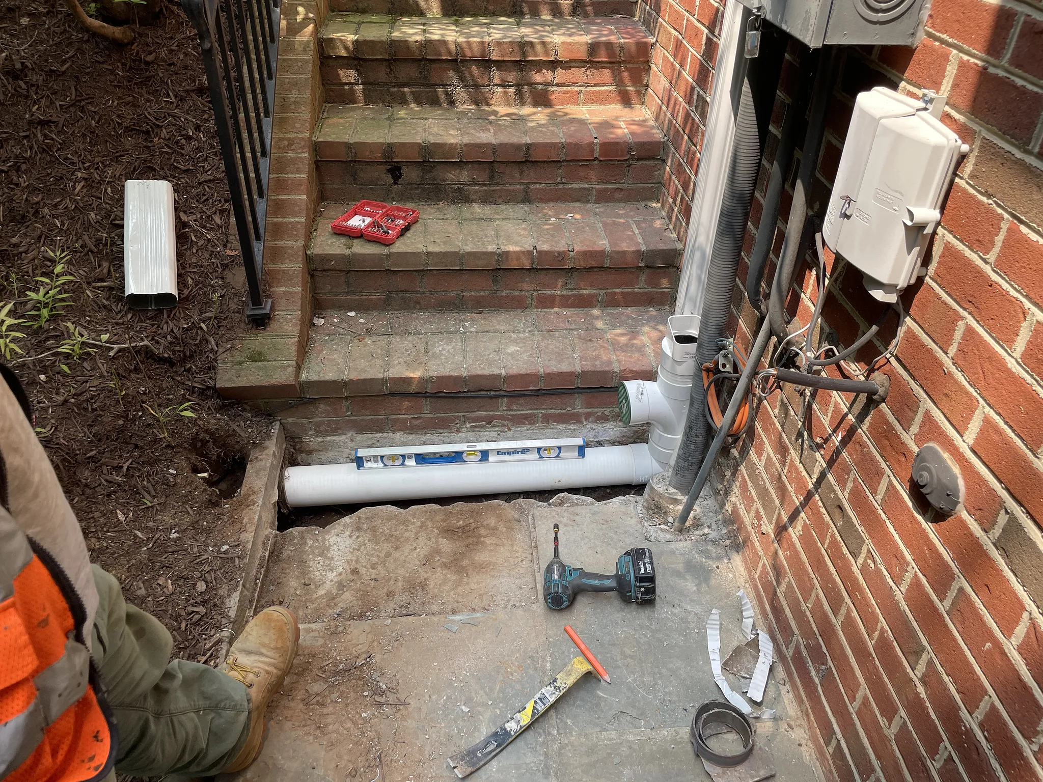 Solid PVC pipe installed in an opened concrete entryway beside brick steps at a Potomac MD home
