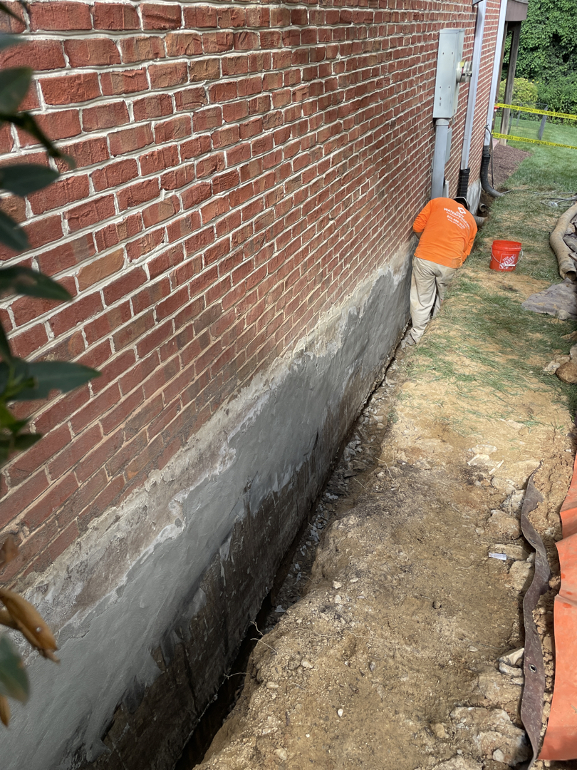 Crew applying gray cementitious waterproofing to an exposed Bethesda foundation wall