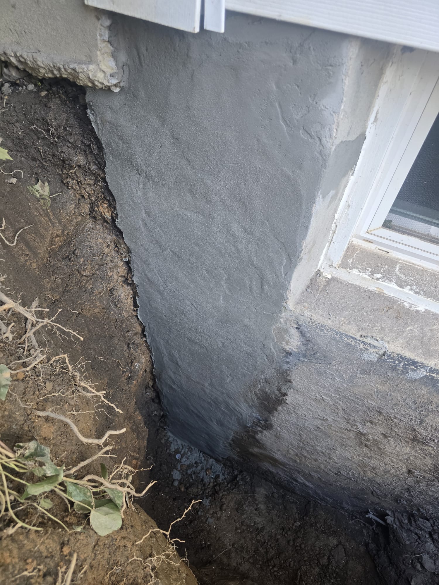 Exterior Waterproofing in Rockville, MD: Windowed Foundation Wall Case 4 Gray cementitious waterproofing coat on the Rockville foundation wall beside a basement window