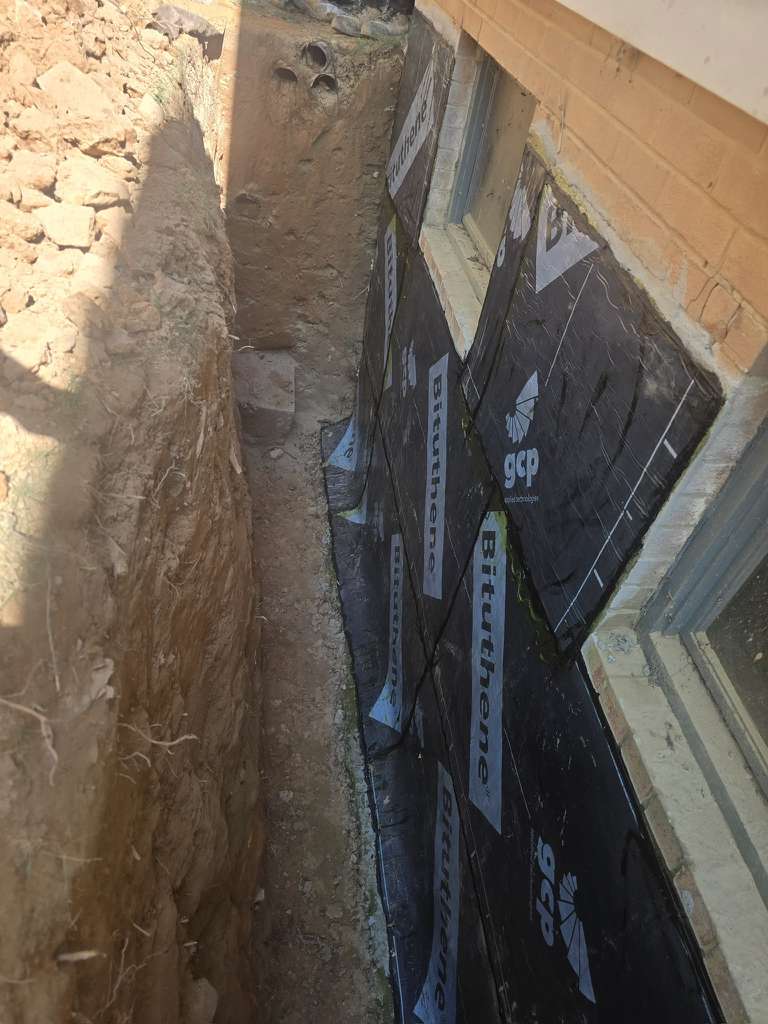 Exterior Waterproofing in Rockville, MD: Windowed Foundation Wall Case 7 Installed sheet waterproofing membrane along the deep foundation trench beneath Rockville basement windows