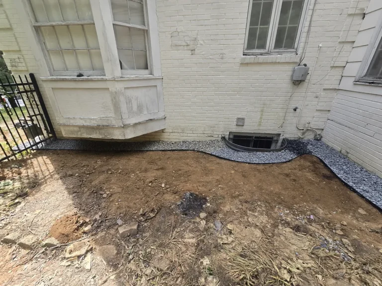 Completed exterior waterproofing and near-grade gravel drainage band around a Bethesda basement window well