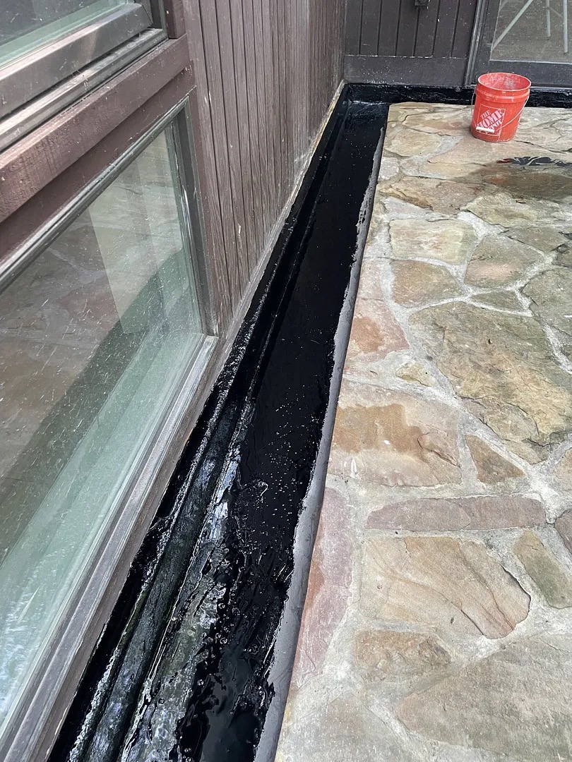 Dark waterproof membrane lining the narrow drainage trench beside the basement extension