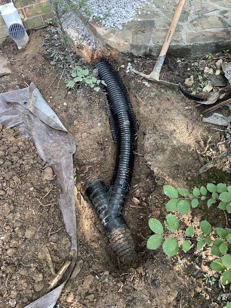 Buried corrugated drainage pipe being installed beyond the patio edge