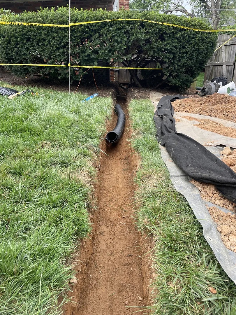 Open yard-drain trench crossing a Potomac backyard away from the house
