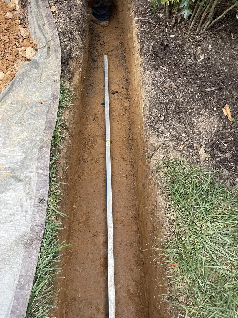 Straightedge and level placed on the bare yard-drain trench bottom to check grade