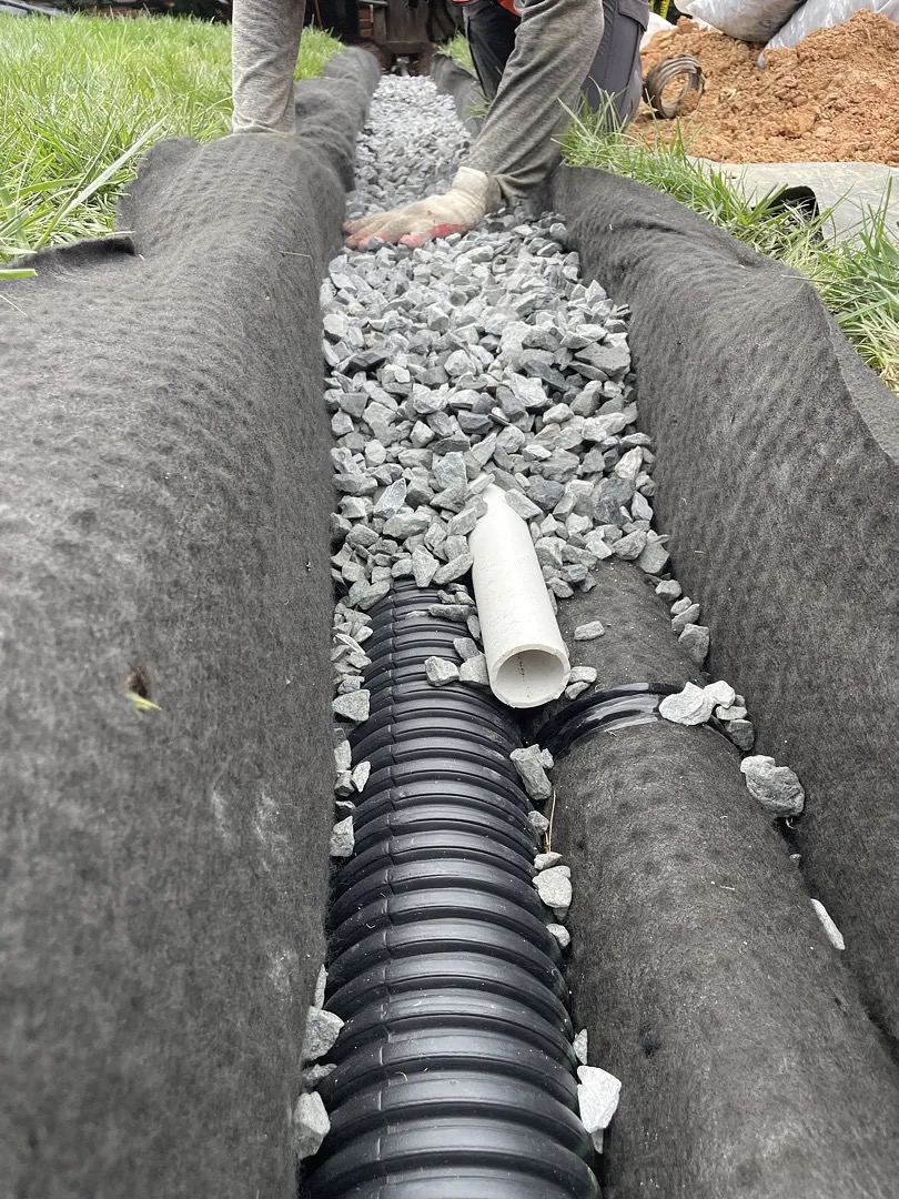 Perforated yard-drain pipe inside a geotextile-lined gravel trench