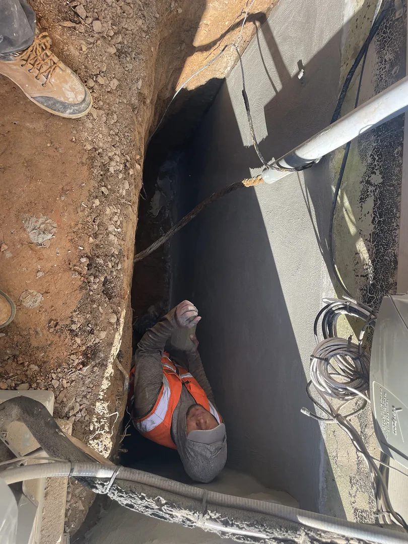 Crew installing sheet membrane along the foundation wall